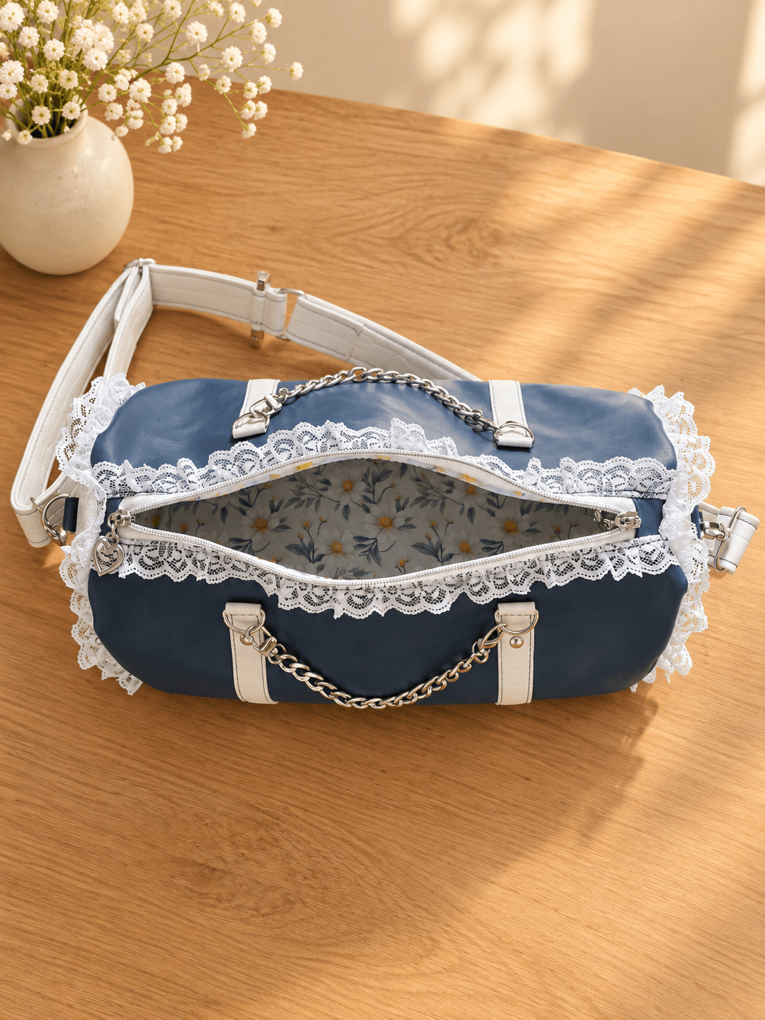 Top view of an open navy handbag with white lace trim, daisy lining, silver-tone chain handles and a white shoulder strap.