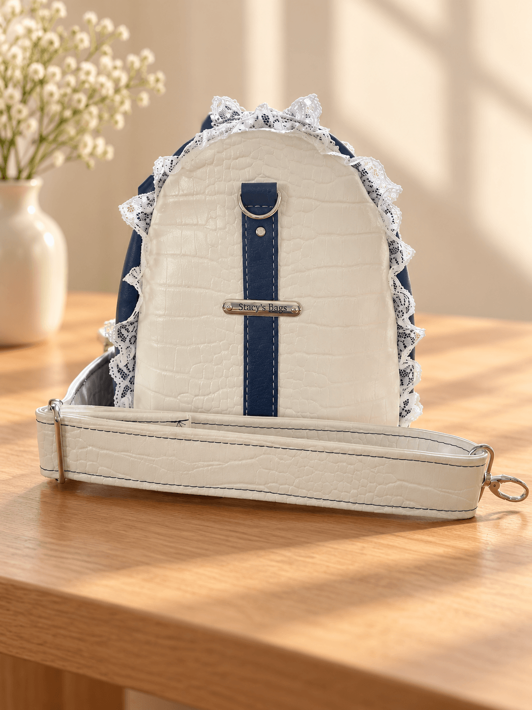 White textured side panel of a navy handbag with lace edging, a navy centre strip, Stacy’s Bags tag and white strap.