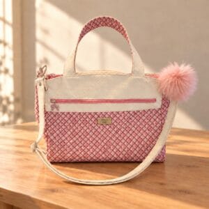 Front of a handmade pink plaid handbag with white textured trim, carry handles, an adjustable strap and a pink pom-pom.